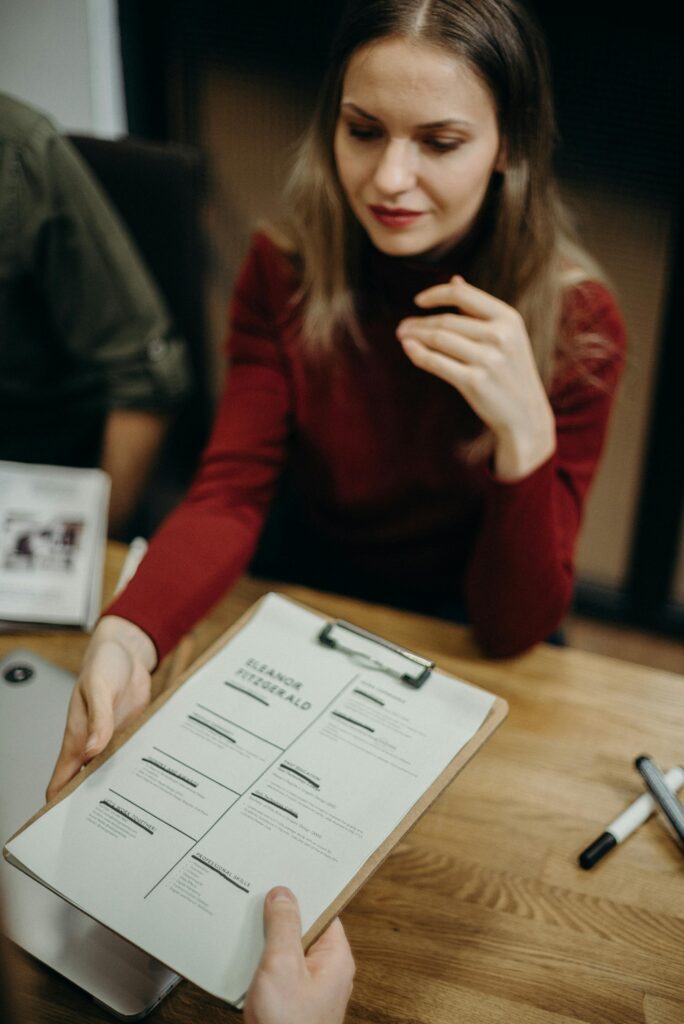pexels photo 3205566 3205566 Woman sitting at a desk holding a clipboard and reviewing a resume during a job interview.