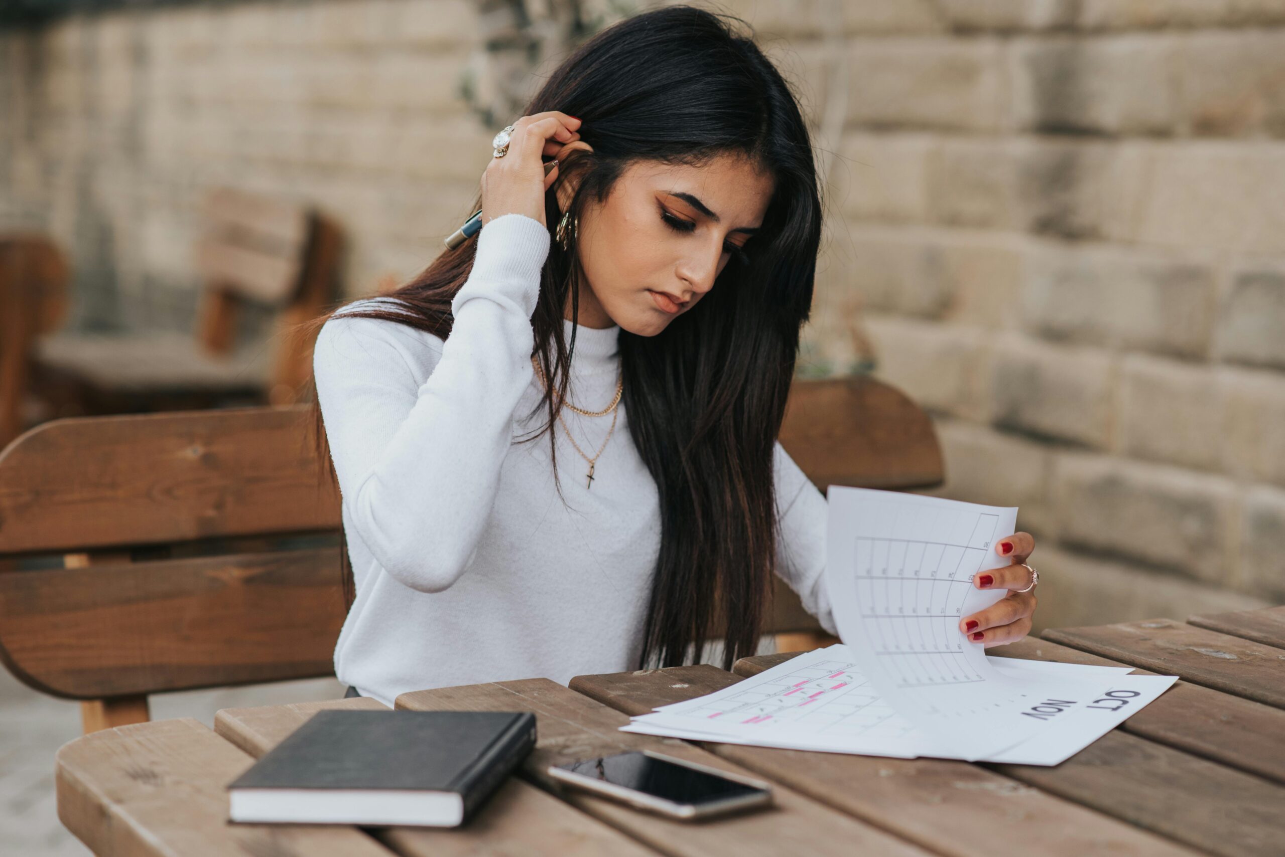 Young ethnic female student in casual outfit with dark hair at wooden table looking through plans in calendar