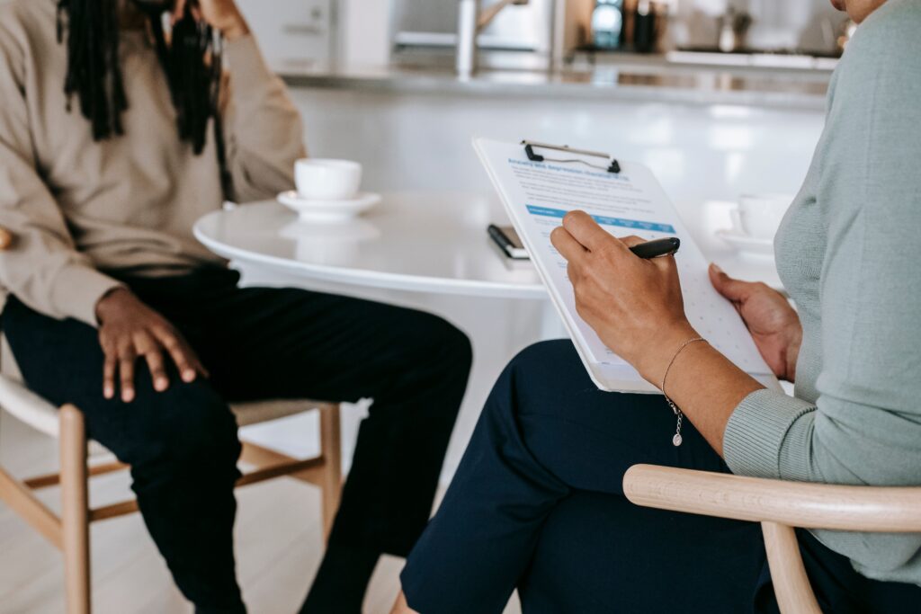 pexels photo 5699475 5699475 Crop unrecognizable female psychotherapist or interviewer asking questions and taking notes in clipboard during interview with black male
