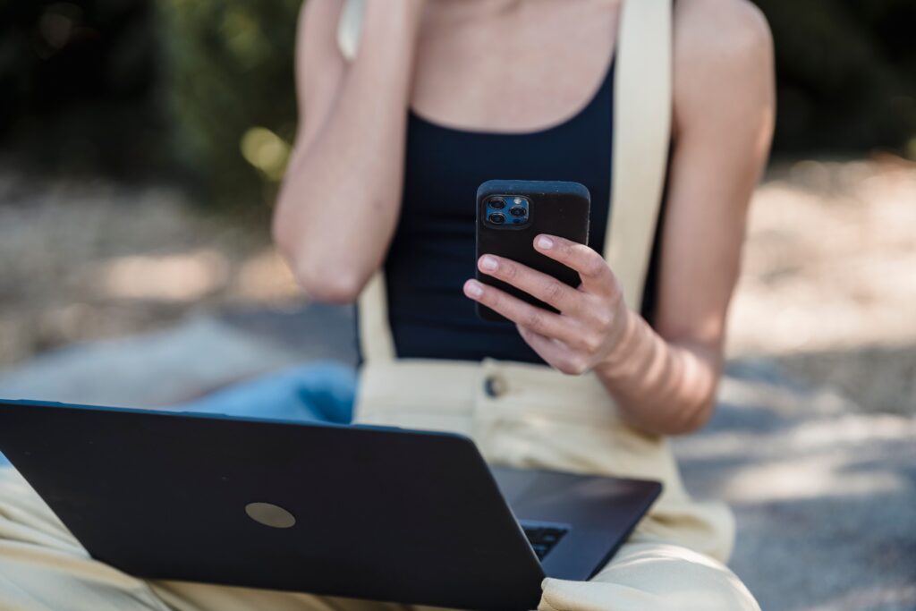 pexels photo 7243024 7243024 Crop unrecognizable woman with bare shoulders sitting outdoors with laptop and using mobile phone